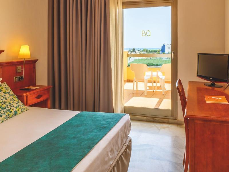 Gemütliches Schlafzimmer mit Doppelbett, Holzmöbeln und Balkon mit Blick auf das Meer.