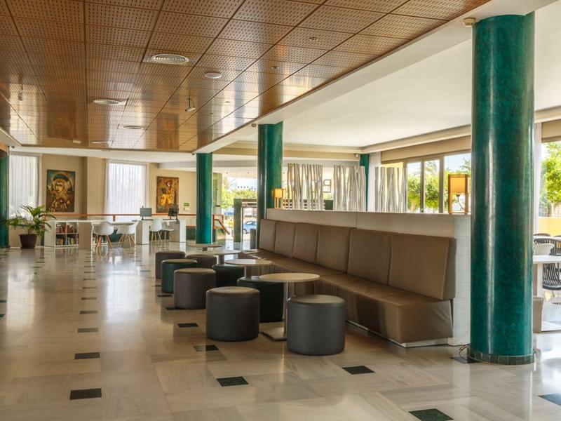 Heller, großzügiger Raum mit Holzdecke, grünen Säulen und Sitzsäcken neben Fensterfronten.