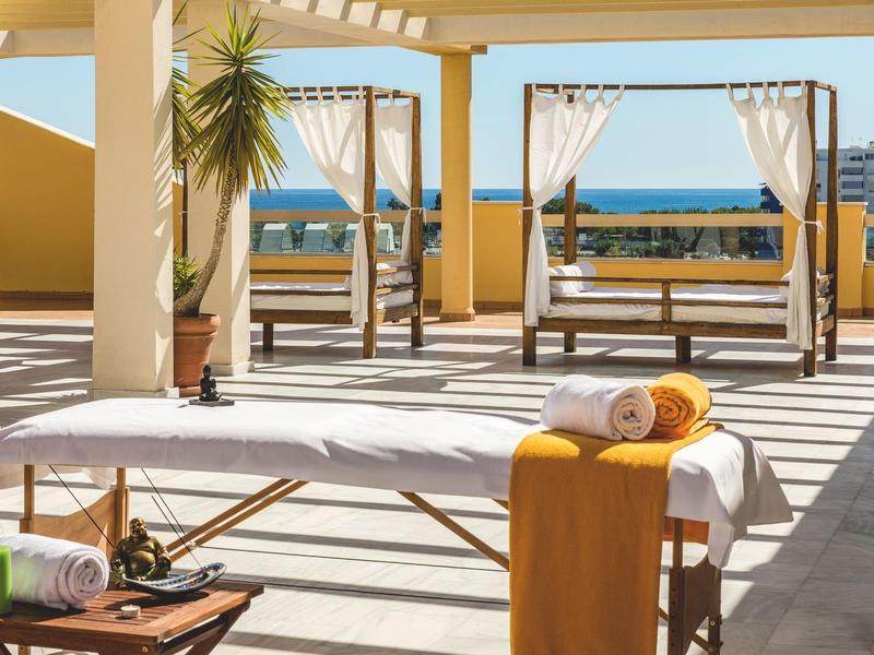 Hell beleuchtete Terrasse mit Massageliege, handtüchern und Blick aufs Meer unter blauen Himmel.