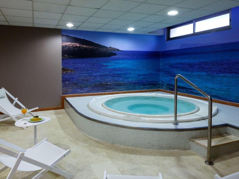 Innen-Whirlpool mit runder Form, Treppe, weißen Liegestühlen und Wandbild eines Meeres.