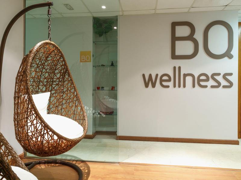 Moderner Wellness-Bereich mit hängendem Korbsessel und bequemen weißen Kissen an heller Wand.