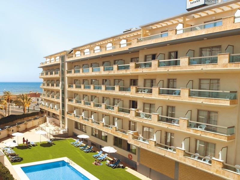 Mehrstöckiges Hotel mit Balkonzimmern, großem Pool und begrünter Liegewiese bei klarem Himmel.