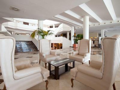 Helle Lounge mit hohen Sesseln, Glastisch und Treppe im Hintergrund, modernes Design.