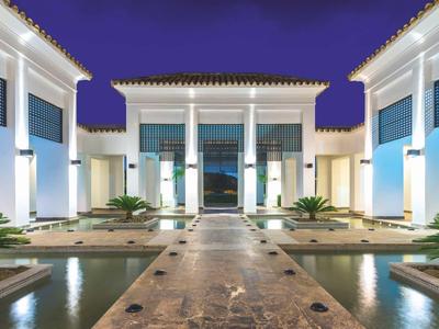 Moderner Gebäudekomplex mit weißer Fassade, Säulen, Wasserbecken und Abendbeleuchtung.