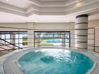 Innen-Whirlpool mit bläulichem Wasser, rundem Becken, großer Fensterfront und weißem, modernem Design.