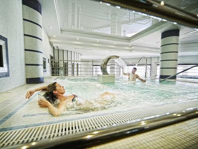 Zwei Frauen entspannen sich in einem modernen Hallenbad mit bequemen Wasserliegen und hellem Ambiente.
