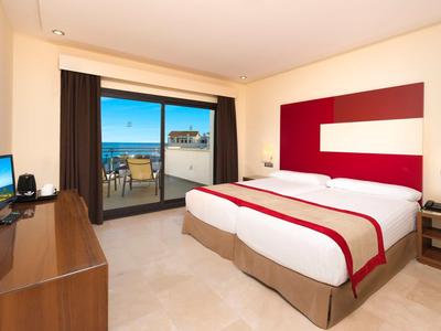 Modernes Hotelzimmer mit großem Doppelbett, Balkon, Meerblick und Schreibtisch mit Fernseher.