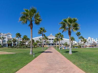 Grand hôtel avec des bâtiments blancs, des palmiers et un ciel bleu clair.