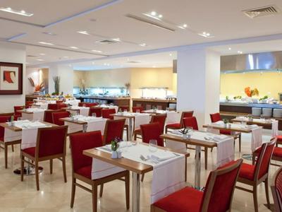 Moderner Speisesaal mit roten Stühlen, weißen Tischdecken und Buffetbereich im Hintergrund.