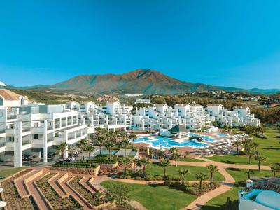 Große weiße Hotelanlage mit Pool, umgeben von grünen Gärten und Bergen im Hintergrund.