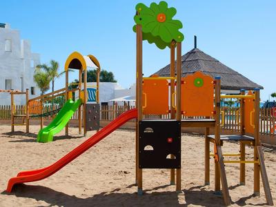 Spielplatz mit buntem Klettergerüst, Rutschen, Sandboden und blauem Himmel im Hintergrund.