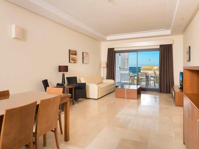 Helles Wohnzimmer mit Essbereich, Sofa, TV, Schreibtisch und Balkon mit Meerblick.