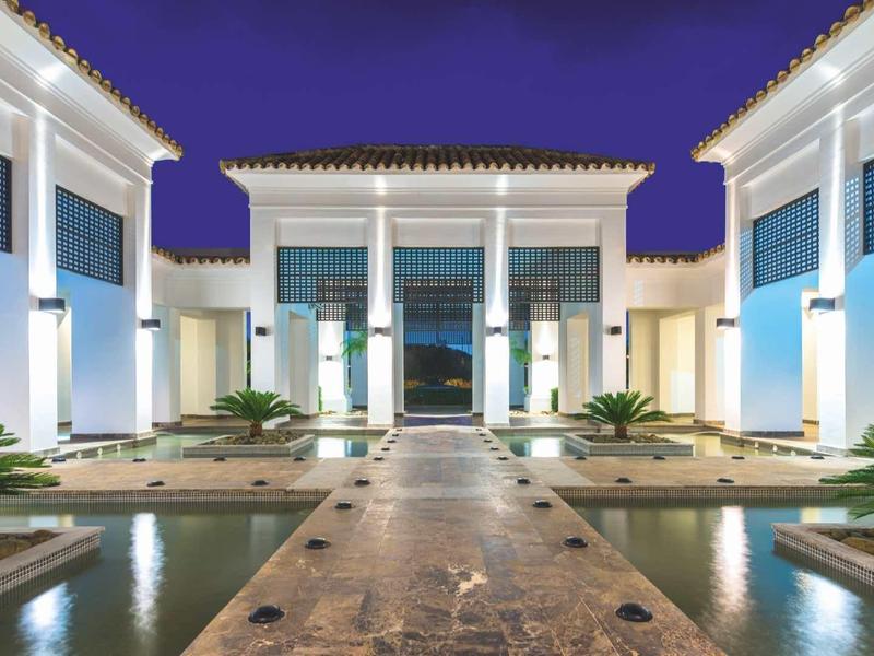 Moderner Gebäudekomplex mit weißer Fassade, Säulen, Wasserbecken und Abendbeleuchtung.