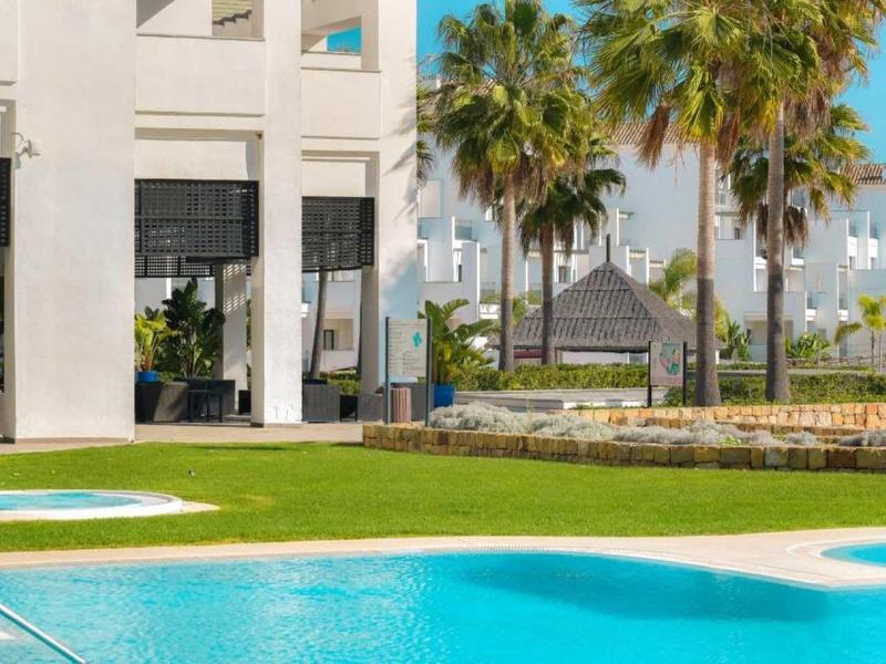 Weißes modernes Gebäude mit großen Fenstern, Palmen und grünem Rasen im sonnigen Außenbereich.