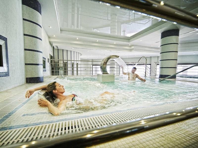 Zwei Frauen entspannen sich in einem modernen Hallenbad mit bequemen Wasserliegen und hellem Ambiente.