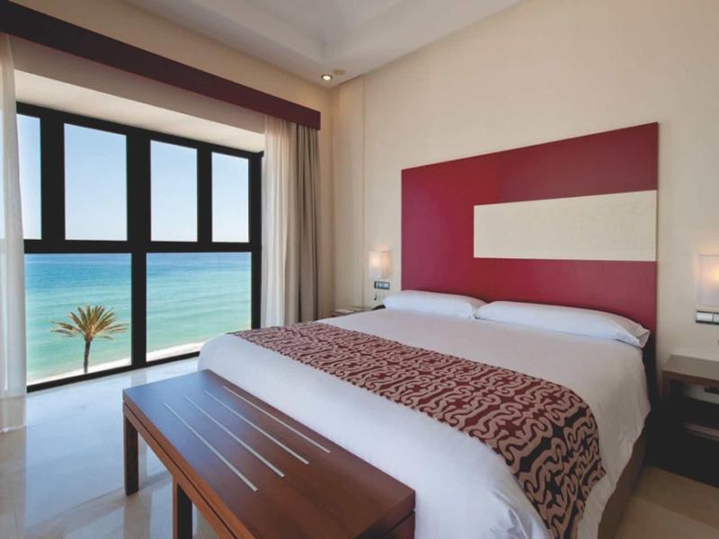 Großes weißes Hotelresort mit Pools, Tennisplatz und Garten in hügeliger, grüner Landschaft.