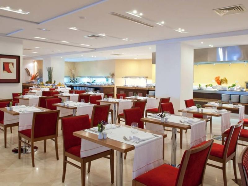 Moderner Speisesaal mit roten Stühlen, weißen Tischdecken und Buffetbereich im Hintergrund.