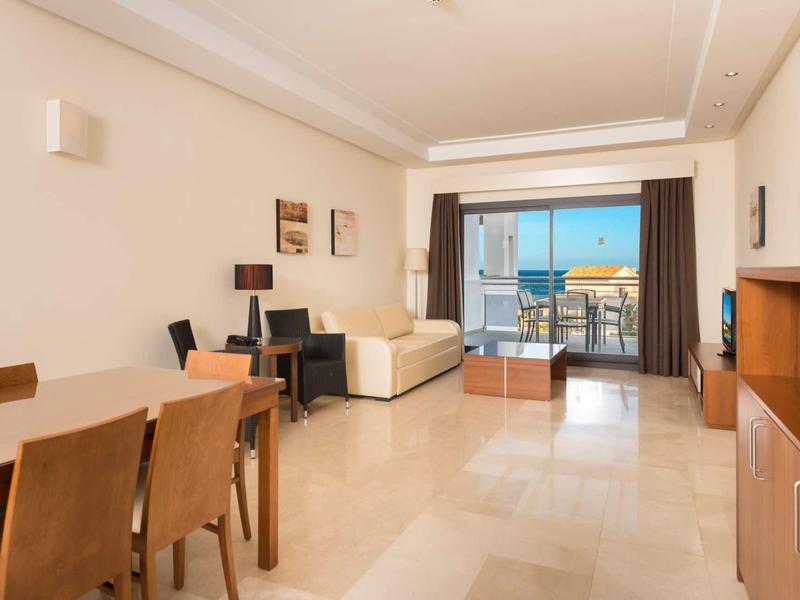 Helles Wohnzimmer mit Essbereich, Sofa, TV, Schreibtisch und Balkon mit Meerblick.