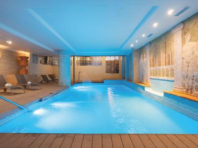 Innen-Pool mit blauem Wasser, Holzverkleidung, Liegestühlen und warmem Deckenlicht.