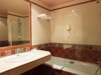 Helles Badezimmer mit Waschbecken, großem Spiegel, Badewanne und braun-roten Wandfliesen.