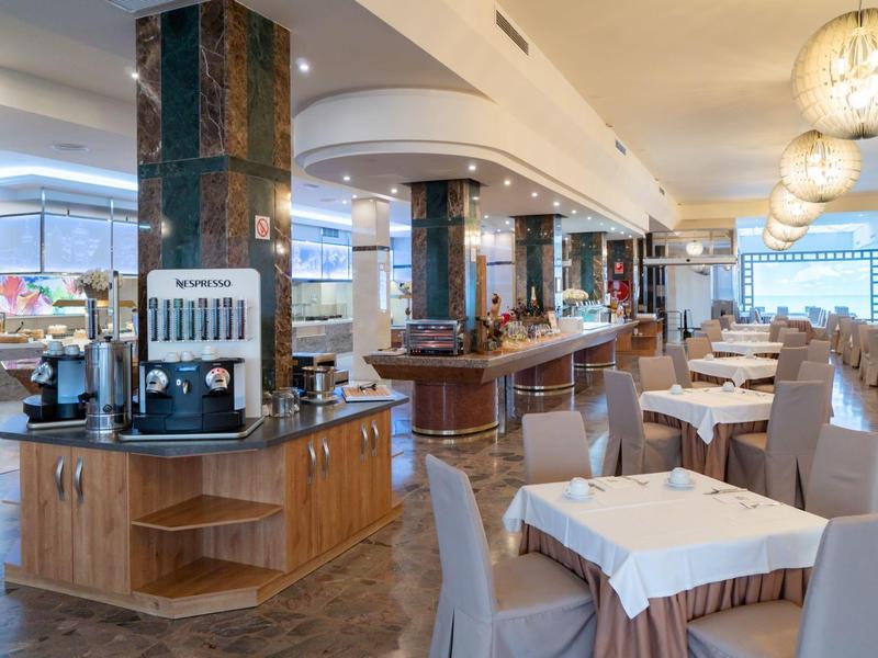 Modernes Restaurant mit beige gedeckten Tischen, grauen Stühlen und einem Getränkestationstisch.