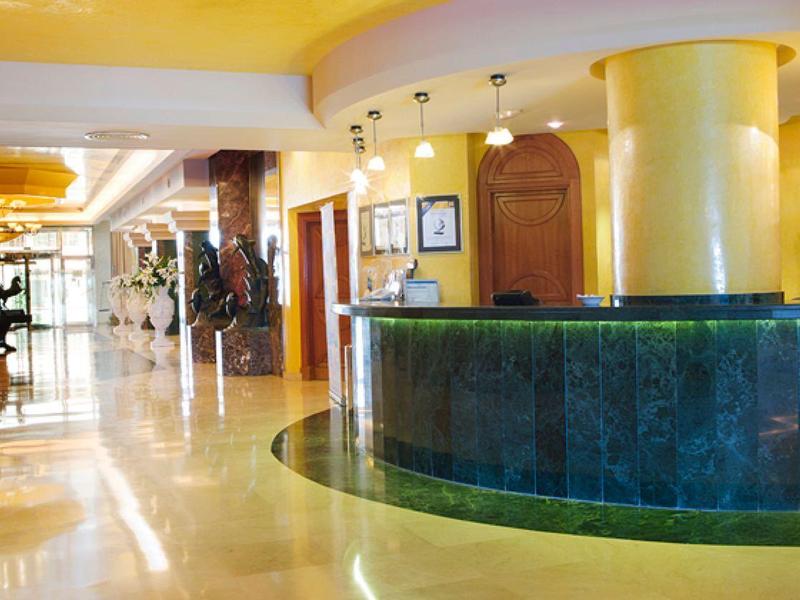 Heller Hotellobby mit rundem grünen Empfangstresen und gelben Wänden, glänzendem Boden.