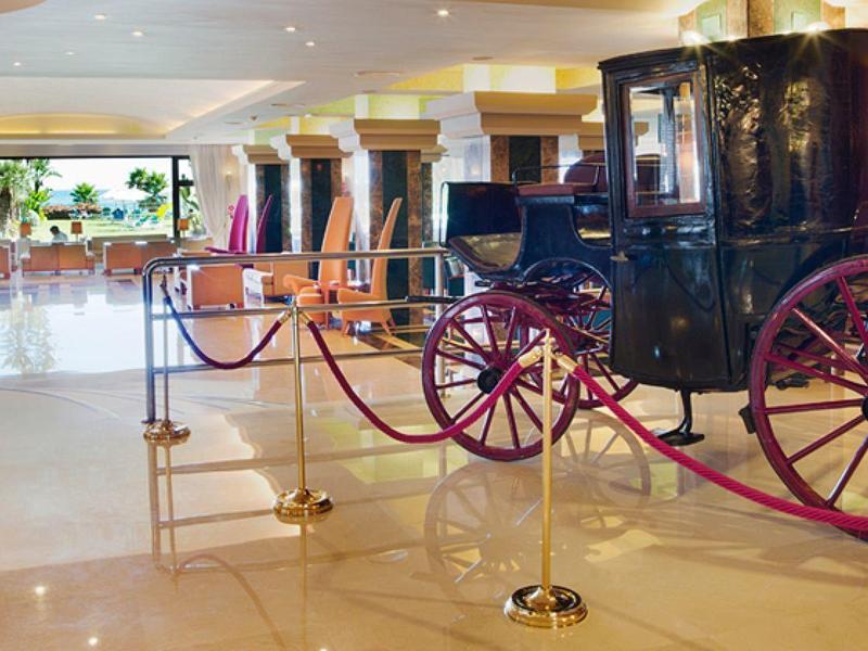 Historische schwarze Kutsche mit roten Speichenrädern in einem hellen Museumssaal.