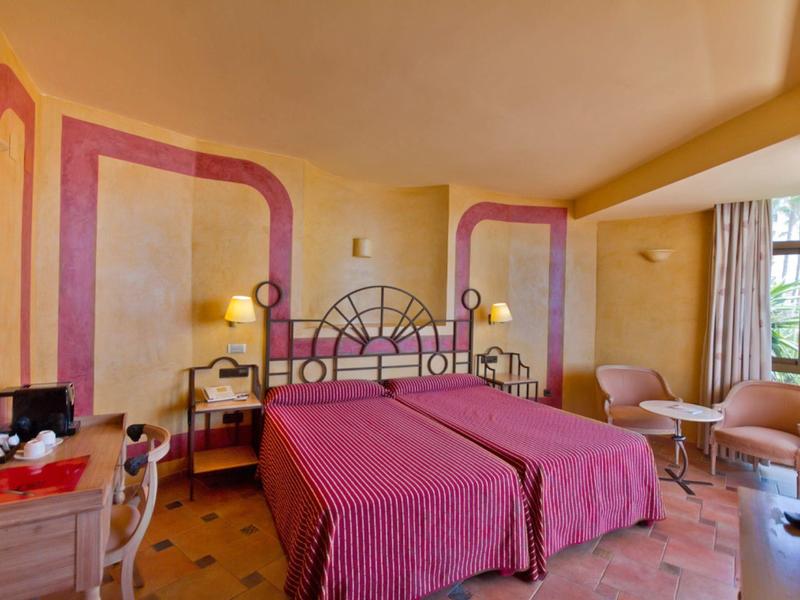 Gemütliches Hotelzimmer mit zwei Einzelbetten, rosa Wänden, Schreibtisch und Sitzecke am Fenster.