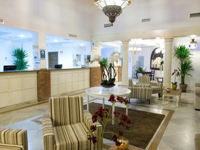 Helle Hotel-Lobby mit gestreiften Sesseln, Orchideen, Teppich und hellem Tresenbereich.