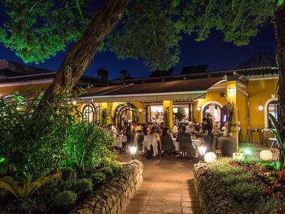 Oświetlona restauracja z gośćmi na tarasie w hotelowym ogrodzie nocą.