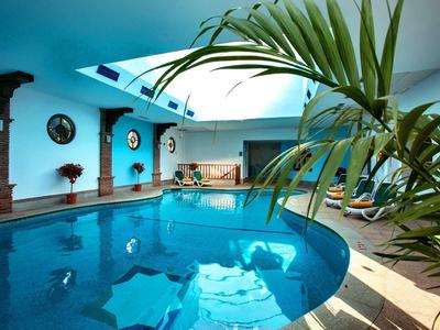 Innen-Schwimmbad mit rundem Becken, blauen Wänden, Pflanzen und Liegestühlen am Rand.