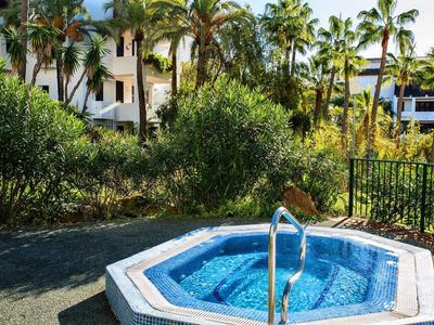 Kleiner blauer Whirlpool im Freien, umgeben von Grün und Palmen vor einem weißen Gebäude.
