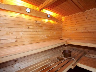 Innenraum einer Holzsauna mit Holzbänken, Saunaeimer und Kelle, warmes Licht an der Decke.