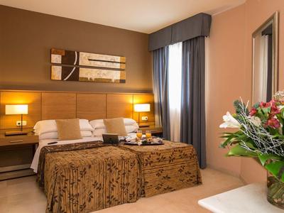 Gemütliches Doppelzimmer mit braunem Kopfteil, Nachtlampen, Kunst an der Wand und Blumen auf Tisch.