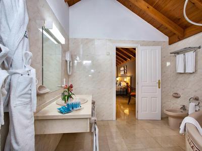 Helles Bad mit Holzbalkendecke, weißer Wand, Waschbecken, Badewanne und Bademänteln am Haken.