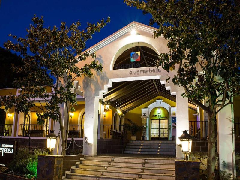 Beleuchteter Hauseingang mit Stufen, Bogen und Bäumen bei Nacht vor dunklem Himmel.