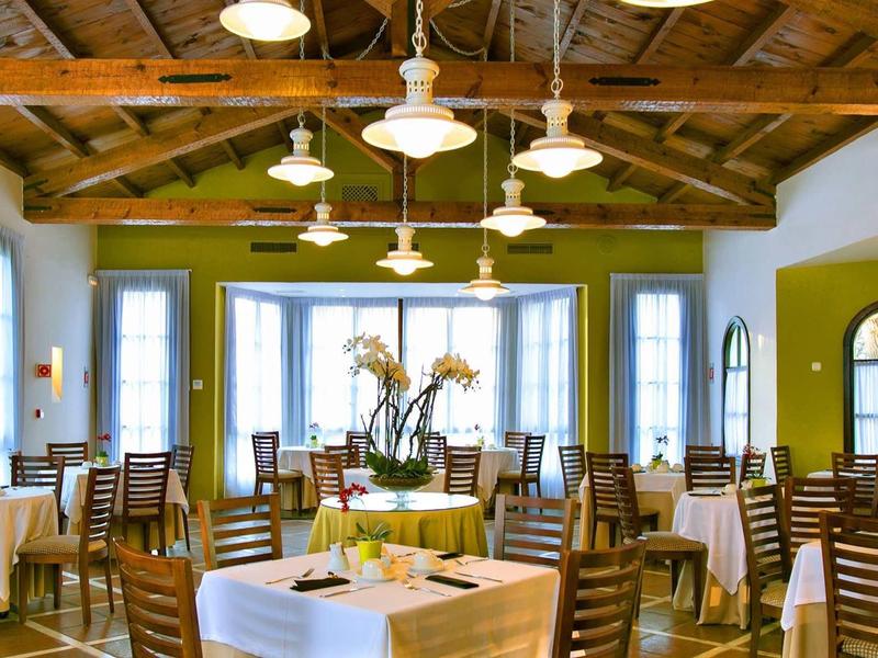 Helles Restaurant mit Holzbalkendecke, weißen Wänden, großen Fenstern und hölzernen Stühlen.