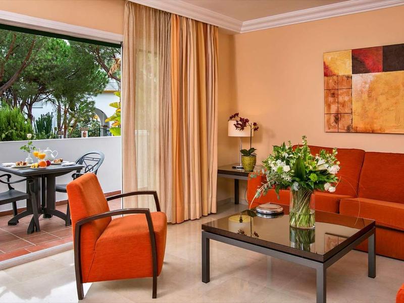 Gemütliches Wohnzimmer mit orangefarbenen Möbeln, Glas-Couchtisch und großer Terrasse mit Gartentisch.