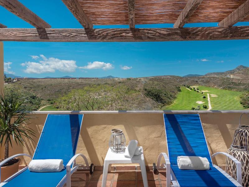 Terrassenblick mit zwei blauen Liegestühlen, kleinem Tisch, Pflanzen und grüner Landschaft im Hintergrund.