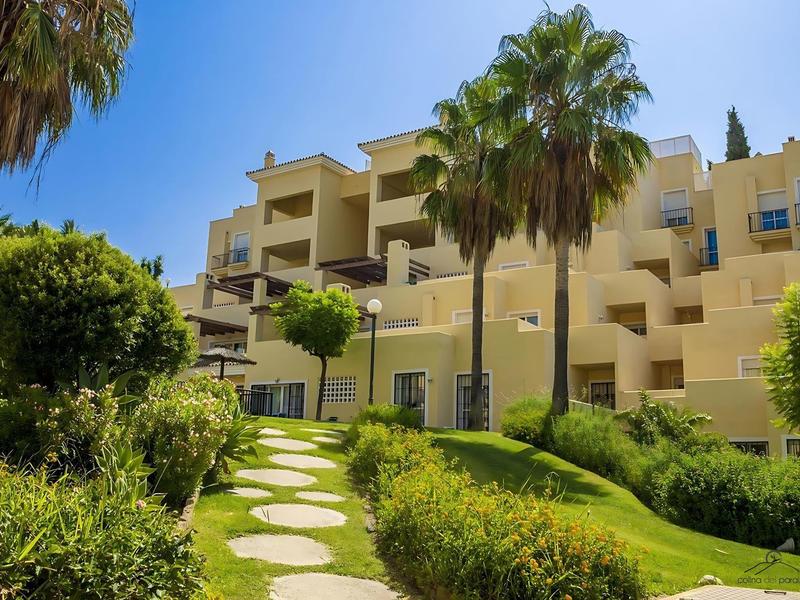 Mehrstöckiges, hellgelbes Gebäude mit Balkonen, umgeben von grünen Palmen und gepflegtem Garten.