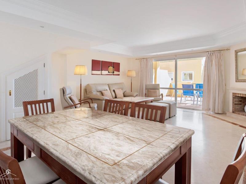 Heller Wohnraum mit Marmor-Esstisch, braunen Stühlen, Sofa, Kamin und Balkon mit blauem Stuhl.