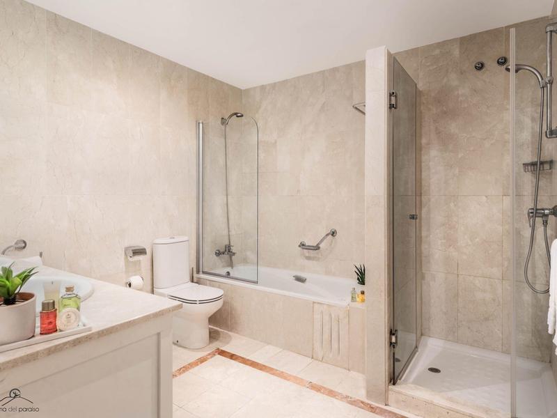 Helles Badezimmer mit Badewanne, Dusche, WC, Waschbecken und hellen Fliesen an Wänden und Boden.