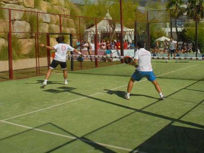Dos hombres juegan al tenis en una pista al aire libre de un hotel en un día soleado.