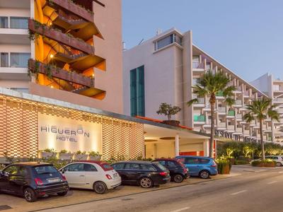 Moderne Hotelfassade mit beleuchtetem Schild und vor dem Gebäude geparkten Autos bei Sonnenuntergang.