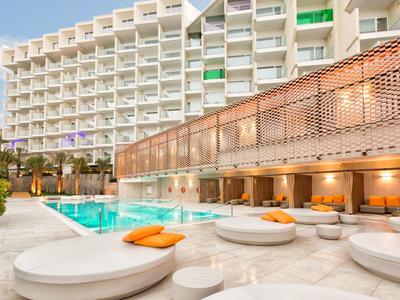 Moderner Hotelaussenpool mit runden Sitzbereichen und orangefarbenen Kissen bei Tageslicht.