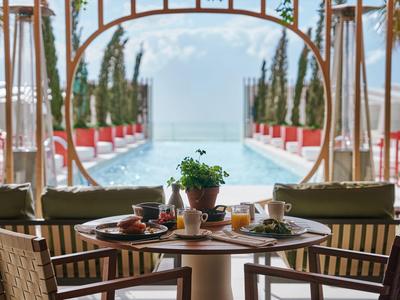 Una mesa elegantemente puesta con vistas a una piscina y el mar bajo un cielo despejado.
