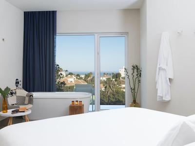 Hell eingerichtetes Hotelzimmer mit großem Fenster und Blick auf das Meer.