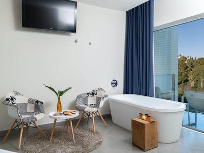 Helles Badezimmer mit freistehender Badewanne, zwei Stühlen, kleinem Tisch und Balkonblick.