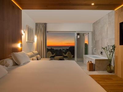 Nowoczesny pokój hotelowy z dużym łóżkiem, wanną i widokiem na zachód słońca.