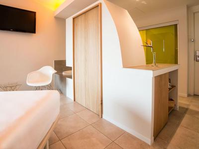 Modernes Hotelzimmer mit Bett, Stuhl, Fernseher und Schrank mit gebogenem Abschluss.